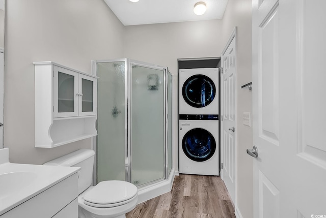 bathroom featuring a shower with shower door, stacked washer and dryer, vanity, hardwood / wood-style flooring, and toilet