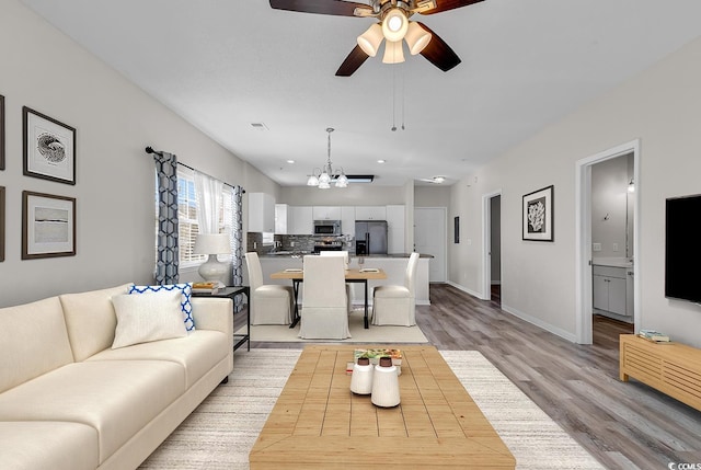 living room with ceiling fan with notable chandelier and light hardwood / wood-style flooring