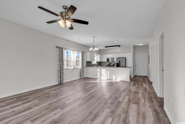 unfurnished living room featuring ceiling fan with notable chandelier and light hardwood / wood-style flooring