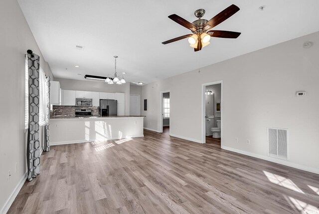 unfurnished living room featuring ceiling fan with notable chandelier and light hardwood / wood-style flooring