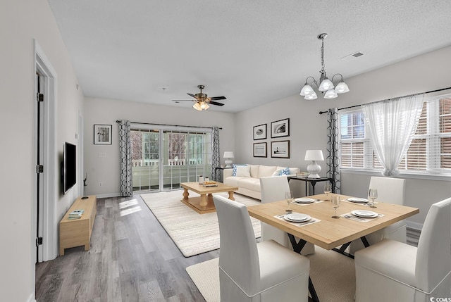 dining room featuring ceiling fan with notable chandelier, wood-type flooring, and a textured ceiling