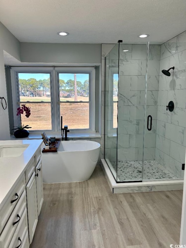 bathroom featuring wood finished floors, a freestanding bath, a textured ceiling, a shower stall, and vanity