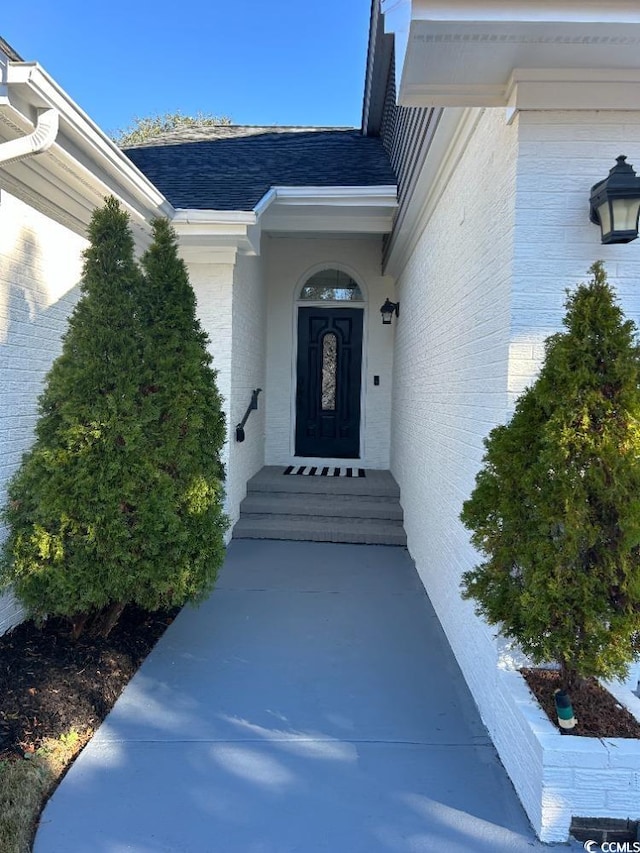 doorway to property with brick siding and roof with shingles