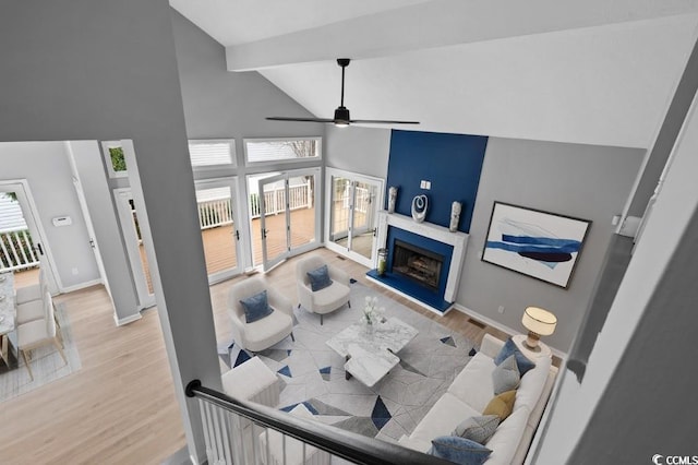 living area with high vaulted ceiling, baseboards, a fireplace with raised hearth, and wood finished floors