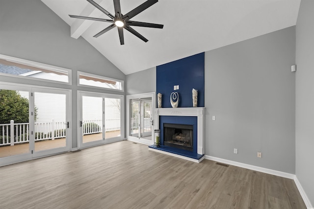 unfurnished living room with a fireplace with raised hearth, high vaulted ceiling, wood finished floors, a ceiling fan, and baseboards