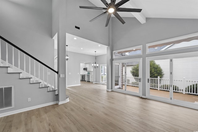 unfurnished living room featuring baseboards, visible vents, wood finished floors, stairs, and ceiling fan with notable chandelier