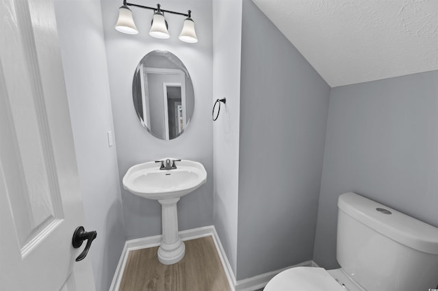 bathroom featuring lofted ceiling, toilet, a textured ceiling, wood finished floors, and baseboards