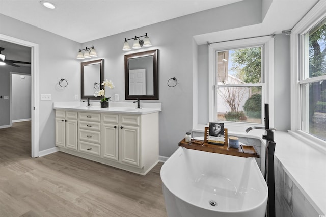 full bath with double vanity, a soaking tub, baseboards, and wood finished floors