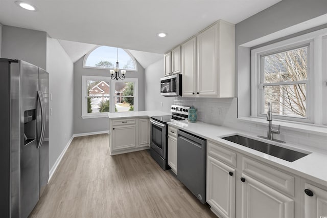 kitchen featuring white cabinets, stainless steel appliances, sink, a chandelier, and lofted ceiling