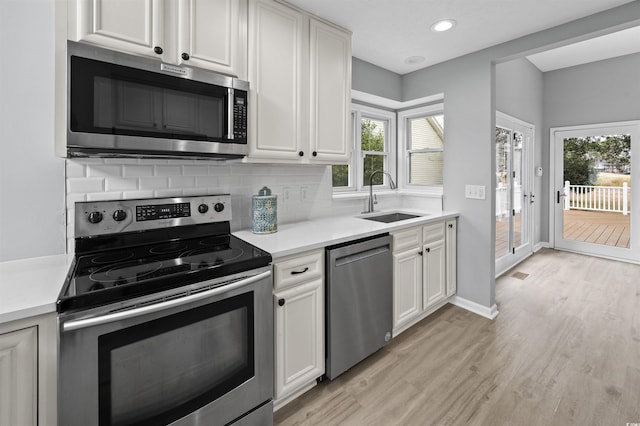 kitchen featuring stainless steel appliances, a sink, light countertops, light wood-type flooring, and decorative backsplash