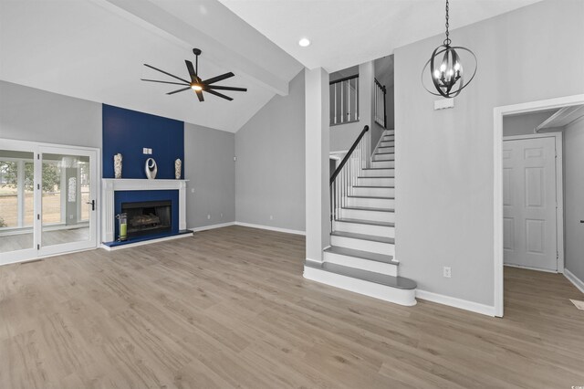 unfurnished living room featuring a fireplace, beamed ceiling, ceiling fan with notable chandelier, and light hardwood / wood-style flooring