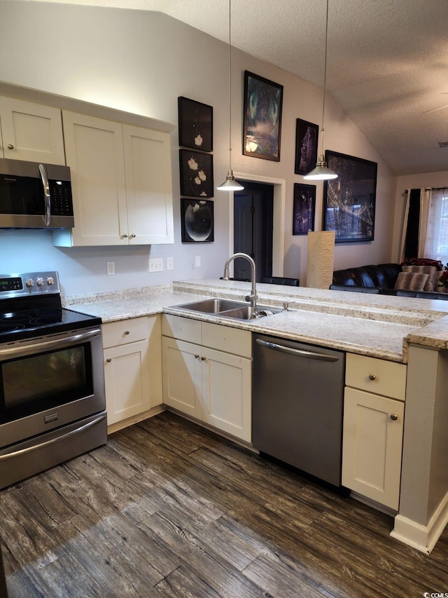 kitchen with a textured ceiling, stainless steel appliances, vaulted ceiling, sink, and decorative light fixtures