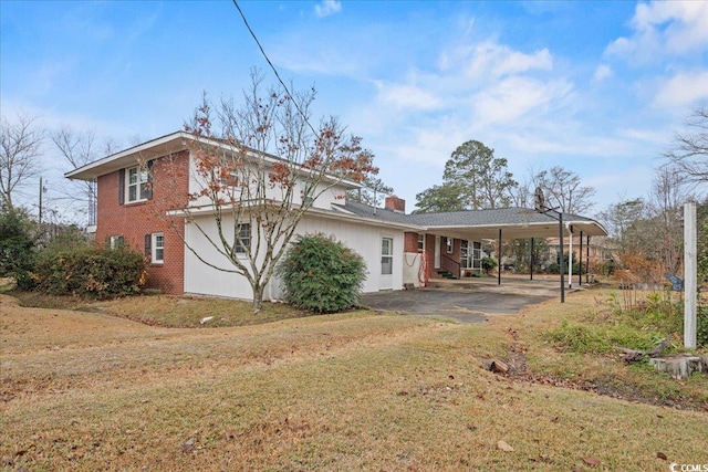 rear view of property with an attached carport, a lawn, a chimney, and brick siding