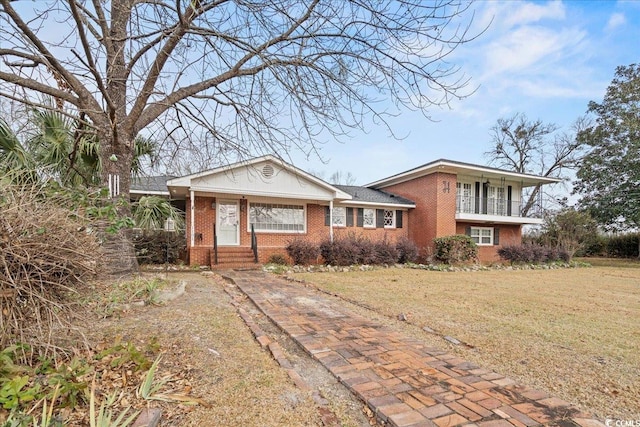 view of front of property featuring a balcony, driveway, a front lawn, and brick siding