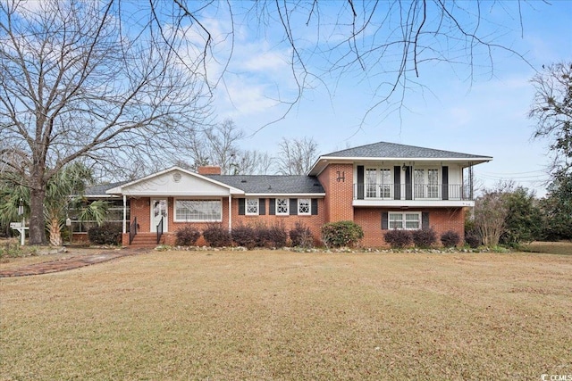 tri-level home with a balcony, brick siding, a chimney, and a front yard