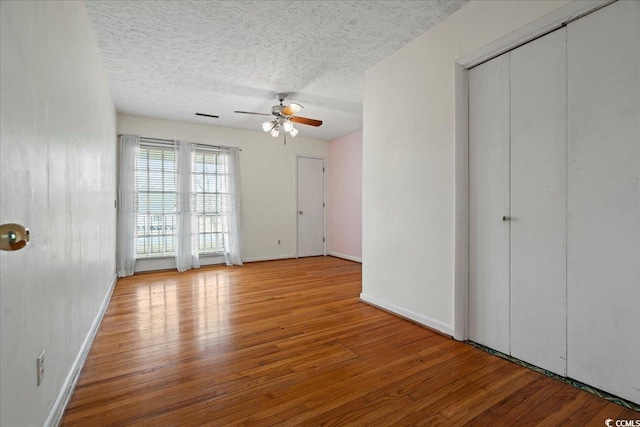 unfurnished bedroom with a textured ceiling, ceiling fan, wood finished floors, visible vents, and baseboards