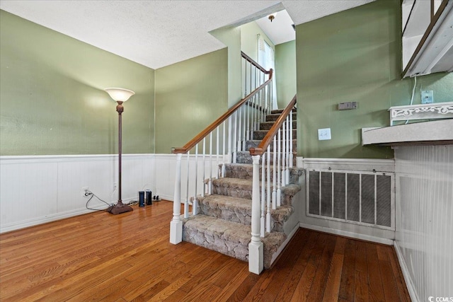 stairs with wainscoting, visible vents, a textured ceiling, and wood finished floors