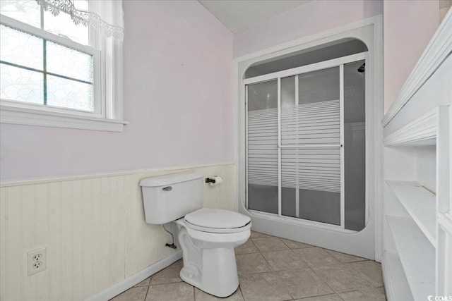 full bath featuring a shower with shower door, wainscoting, toilet, and tile patterned floors