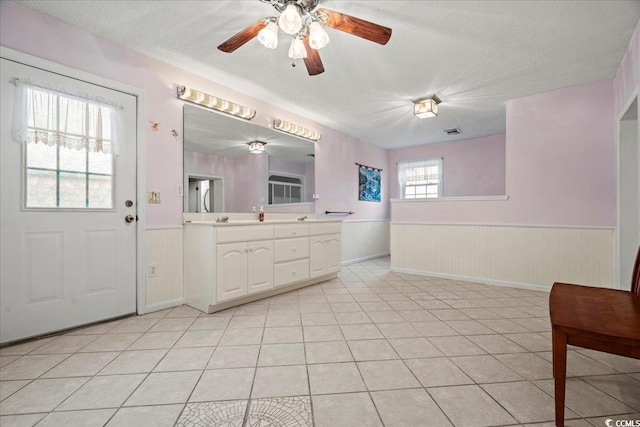 full bathroom with double vanity, wainscoting, tile patterned flooring, a textured ceiling, and a sink