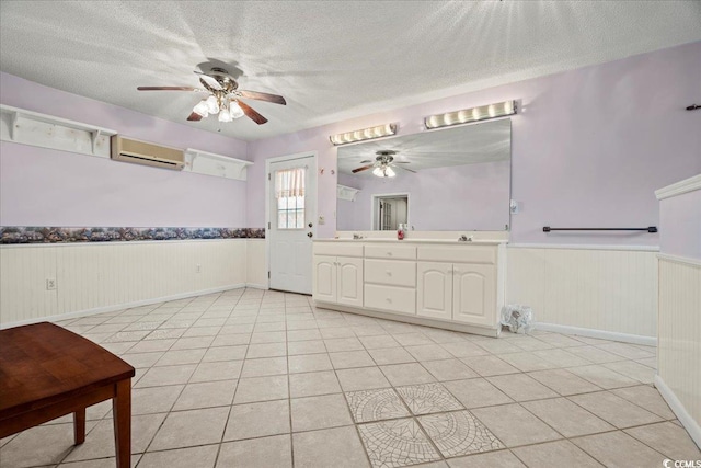 bathroom with a textured ceiling, wainscoting, a wall unit AC, and tile patterned flooring