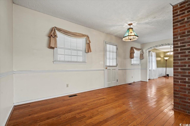 empty room with a healthy amount of sunlight, hardwood / wood-style flooring, visible vents, and arched walkways