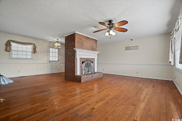 unfurnished living room with hardwood / wood-style floors, a brick fireplace, ceiling fan, a textured ceiling, and baseboards