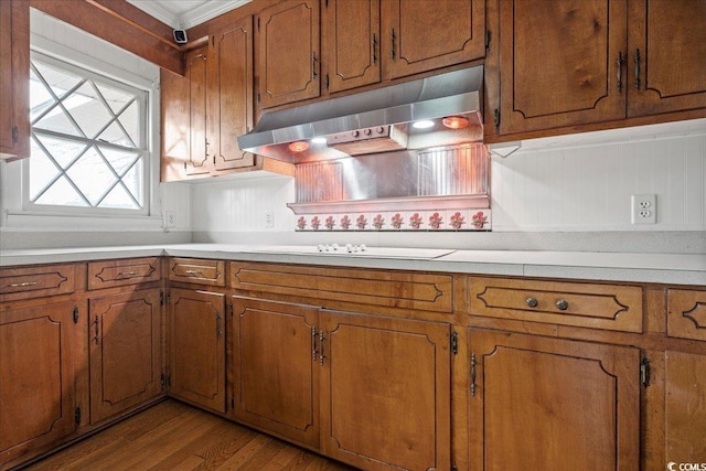 kitchen featuring under cabinet range hood, brown cabinetry, light countertops, and wood finished floors