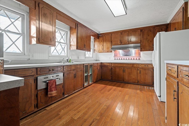 kitchen with brown cabinetry, freestanding refrigerator, and under cabinet range hood