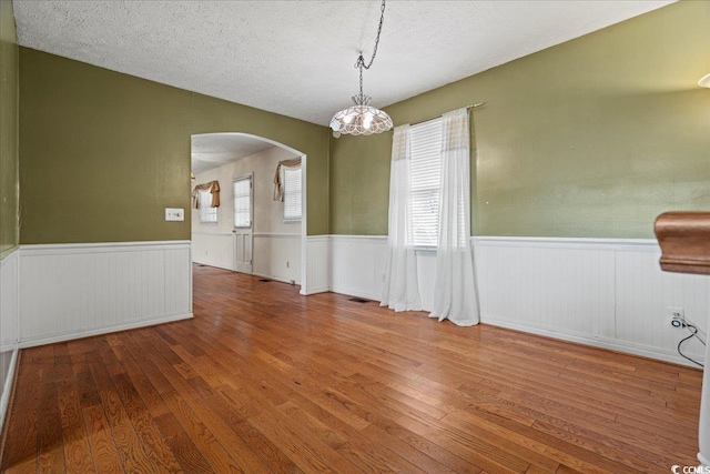 empty room featuring arched walkways, wainscoting, a textured ceiling, and hardwood / wood-style floors