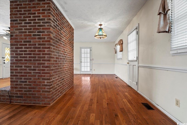 hallway with a textured ceiling, brick wall, wood-type flooring, and visible vents