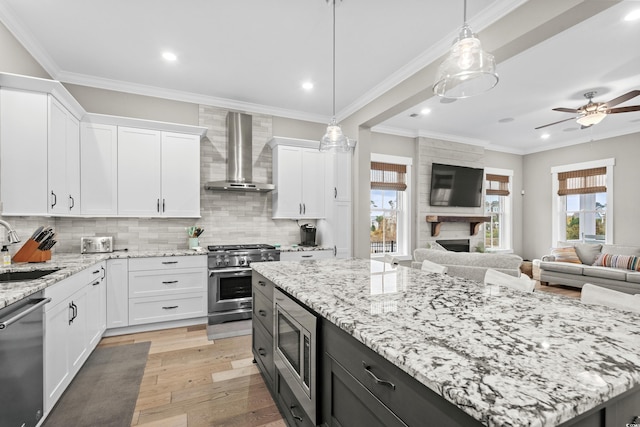 kitchen with appliances with stainless steel finishes, wall chimney exhaust hood, white cabinets, a kitchen island, and hanging light fixtures