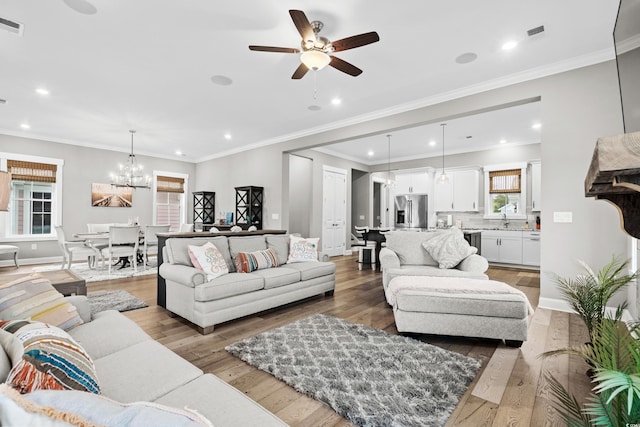 living room featuring wood-type flooring, ceiling fan with notable chandelier, ornamental molding, and sink