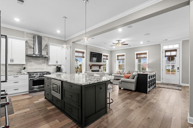 kitchen featuring appliances with stainless steel finishes, light wood-type flooring, wall chimney exhaust hood, white cabinetry, and a kitchen island