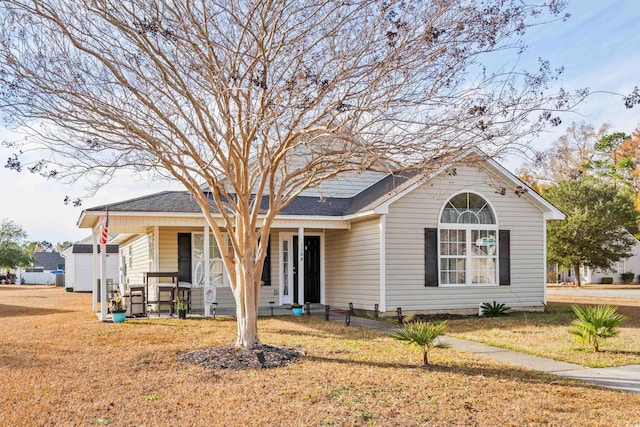 view of front of home with roof with shingles, covered porch, and a front yard