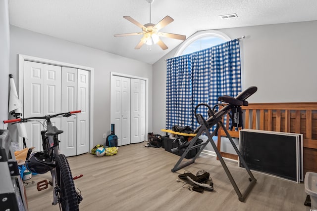 exercise area featuring ceiling fan, a textured ceiling, wood finished floors, and vaulted ceiling