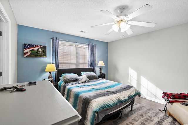 bedroom with visible vents, a textured ceiling, wood finished floors, baseboards, and ceiling fan