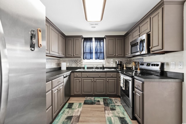 kitchen with a sink, stainless steel appliances, dark countertops, and visible vents