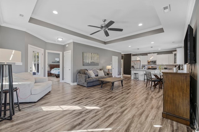 living room featuring ceiling fan, light hardwood / wood-style floors, a raised ceiling, and ornamental molding