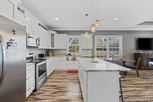 kitchen featuring a center island, white cabinets, sink, appliances with stainless steel finishes, and decorative light fixtures