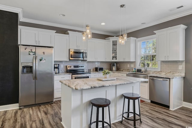 kitchen featuring stainless steel appliances, sink, pendant lighting, a center island, and white cabinetry