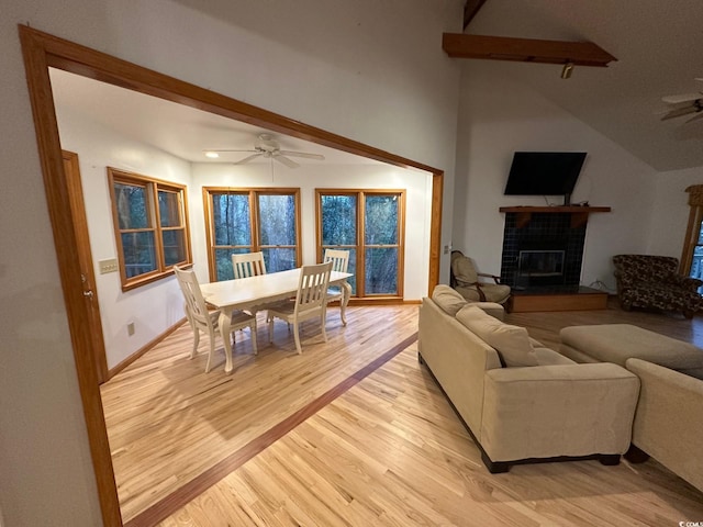 living room with ceiling fan, light hardwood / wood-style flooring, lofted ceiling with beams, and a brick fireplace