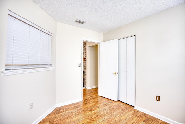 unfurnished bedroom with a textured ceiling, light wood-type flooring, and a closet