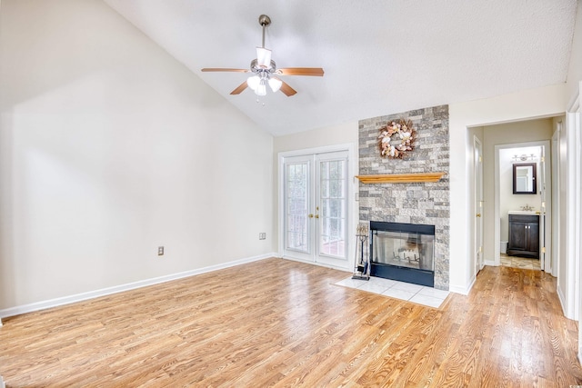 unfurnished living room with high vaulted ceiling, a stone fireplace, light hardwood / wood-style floors, and ceiling fan