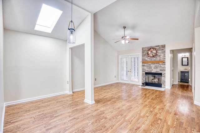 unfurnished living room featuring hardwood / wood-style flooring, lofted ceiling with skylight, a stone fireplace, and ceiling fan