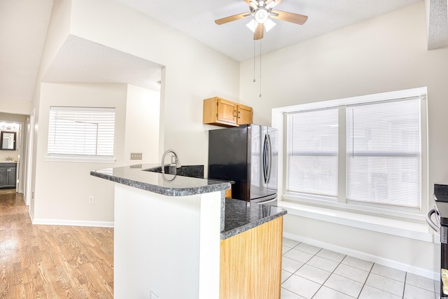 kitchen with light brown cabinetry, light wood-type flooring, stainless steel fridge, kitchen peninsula, and ceiling fan