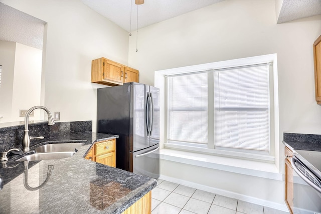 kitchen with sink, stainless steel refrigerator, dark stone countertops, a textured ceiling, and light tile patterned flooring