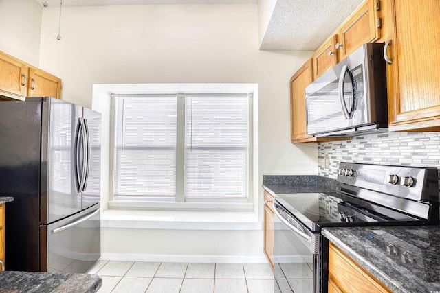 kitchen featuring appliances with stainless steel finishes, tasteful backsplash, dark stone counters, light tile patterned floors, and a textured ceiling