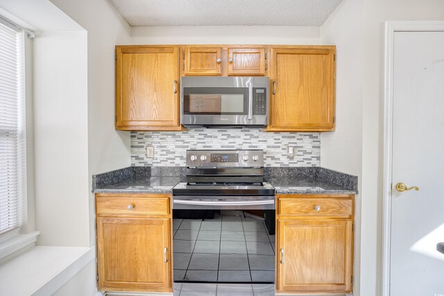 kitchen with dark stone countertops, backsplash, stainless steel appliances, and a textured ceiling