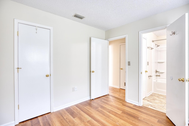 unfurnished bedroom with connected bathroom, light hardwood / wood-style floors, and a textured ceiling