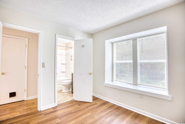 unfurnished bedroom with light hardwood / wood-style floors, a textured ceiling, and ensuite bathroom